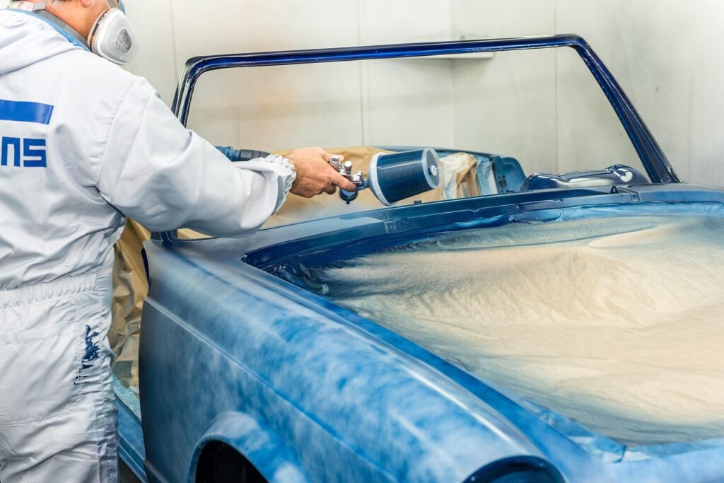 A man in a white suit paints a blue car in Melbourne, showcasing car spray painting skills.
